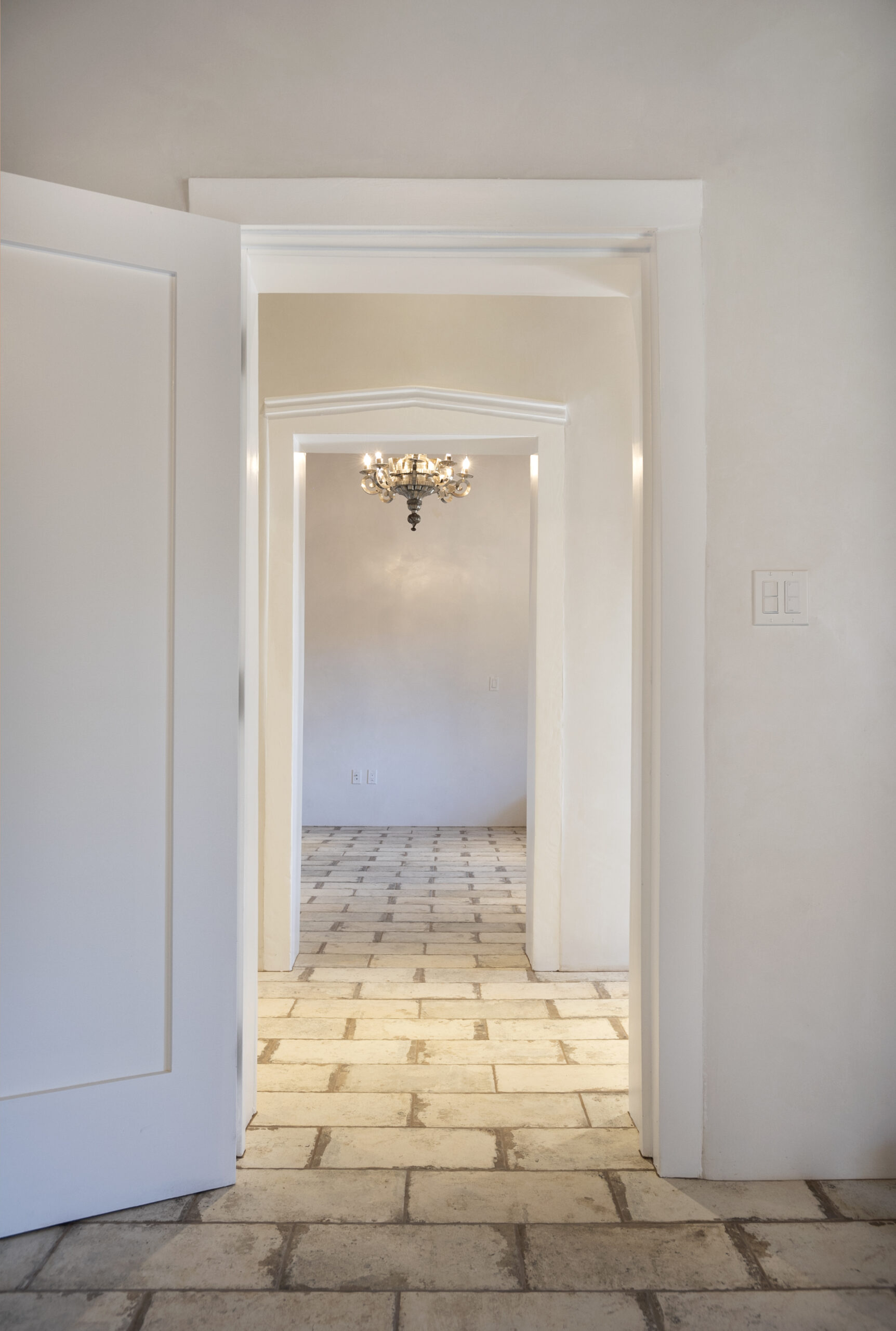 View through a series of open white doors with a chandelier and tiled floor.