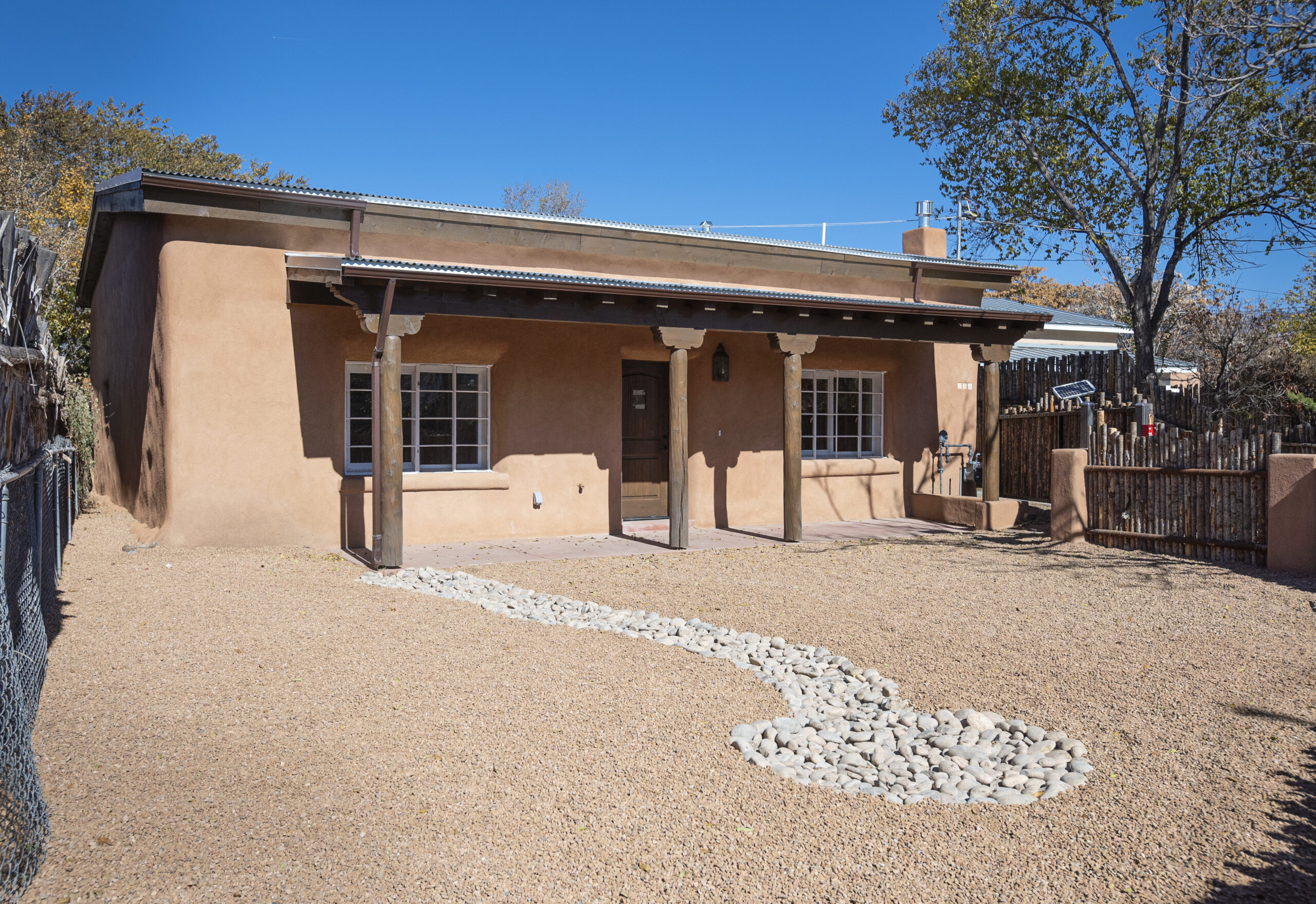 Adobe-style home with wooden porch and gravel yard in sunny setting.