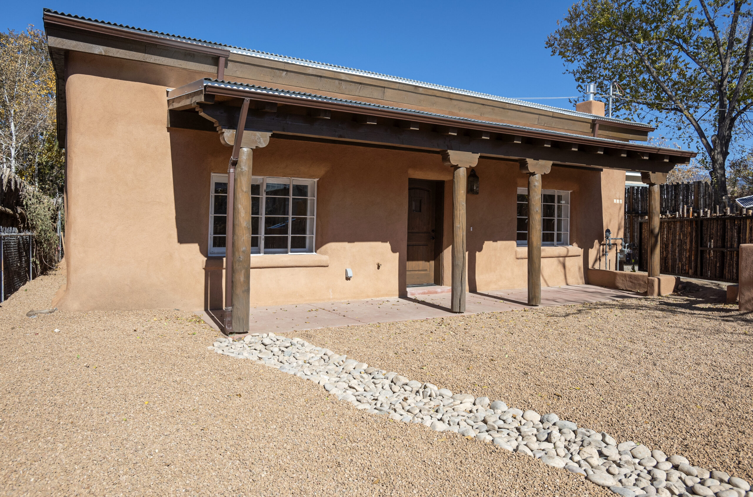 Adobe-style house with wooden pillars and gravel yard under clear blue sky.