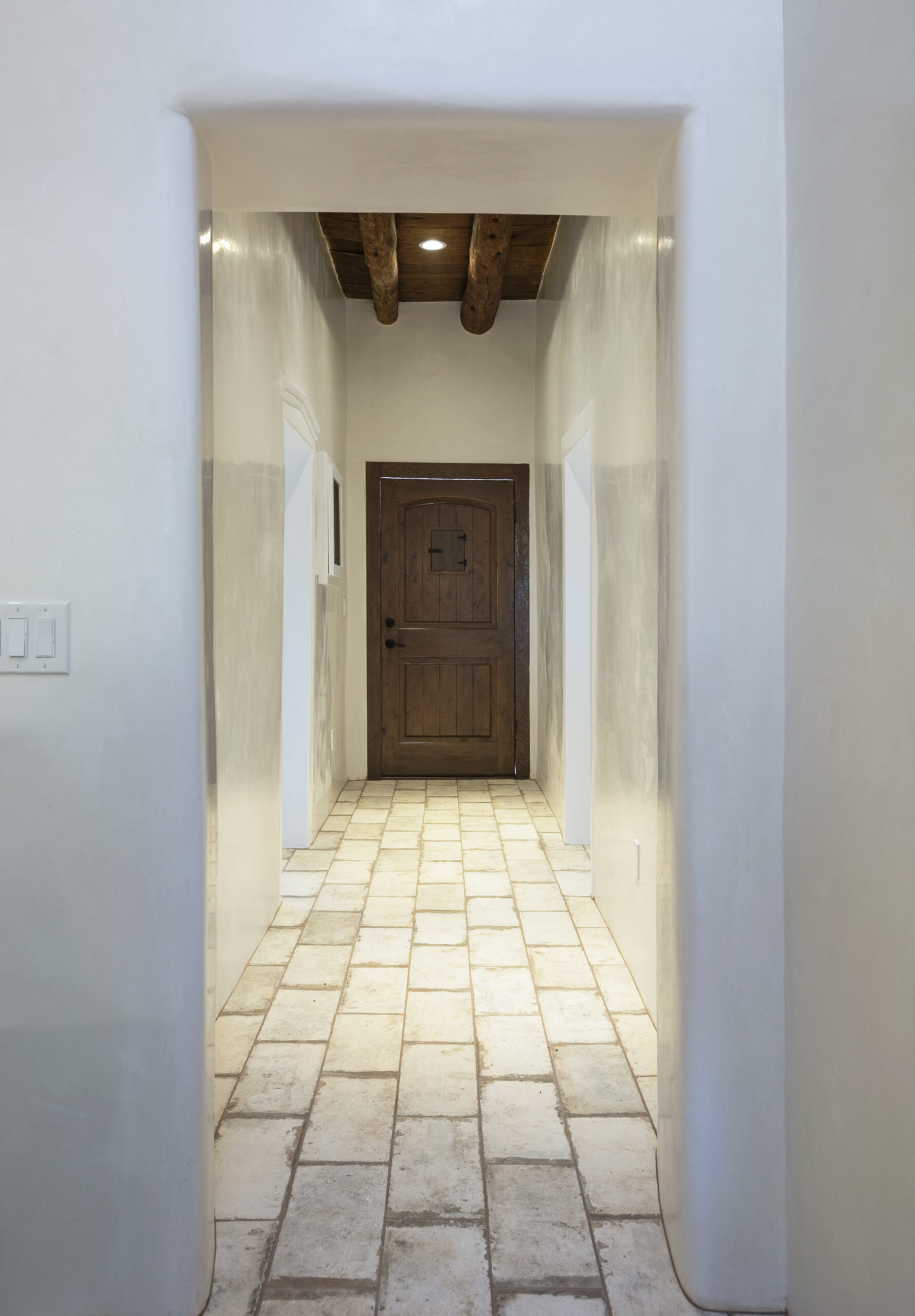 Narrow hallway with beige tiled floor and wooden door at the end.