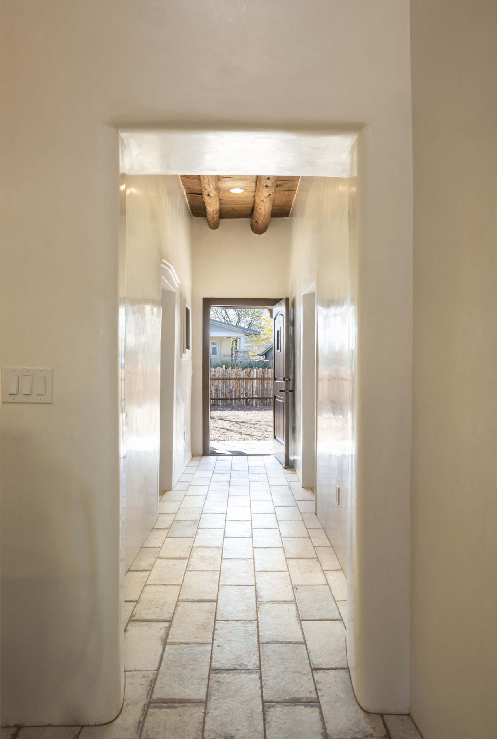 Bright hallway with wooden ceiling beams and tiled floor leading to a balcony.