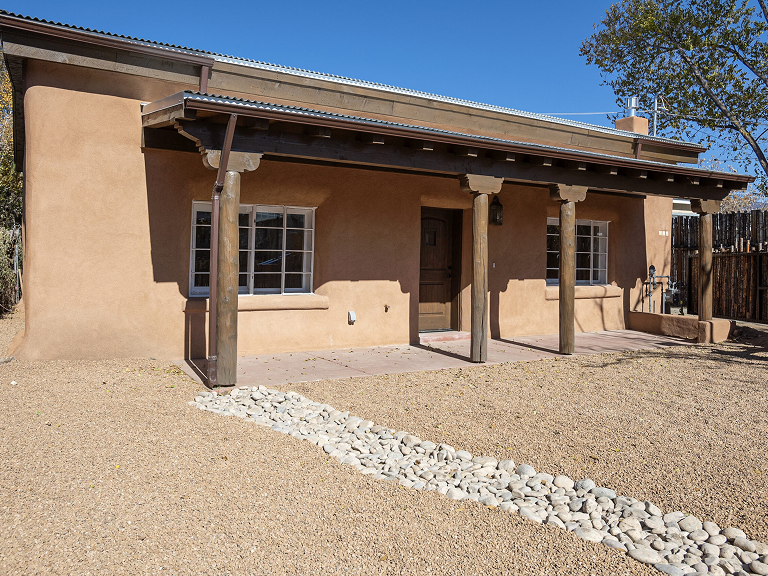 Adobe-style house with wooden pillars and gravel yard under clear blue sky.