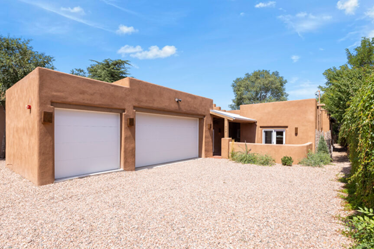 Modern adobe-style house with three garages under a clear blue sky.