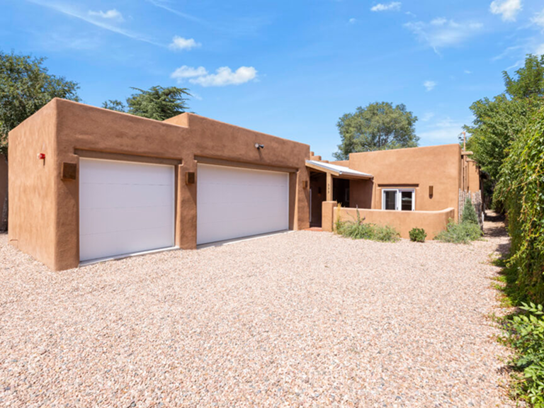 Modern adobe-style house with three garages under a clear blue sky.