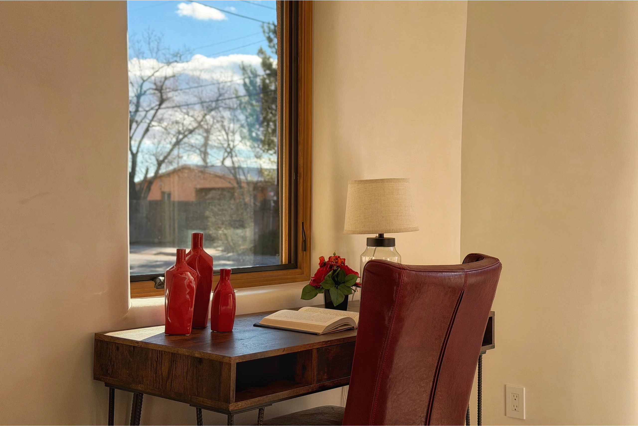 Cozy workspace with red chairs and decorative vases by a sunlit window.