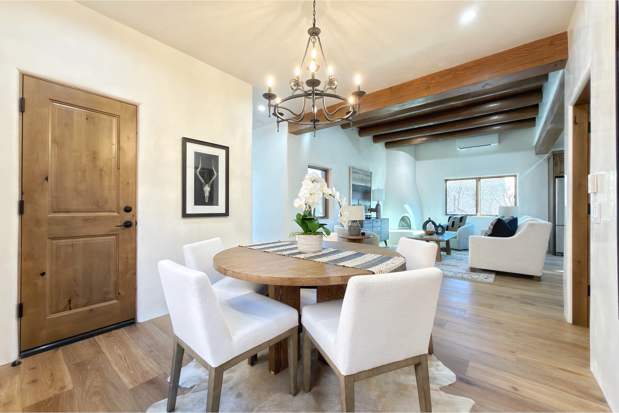 Bright dining area with round wooden table and white chairs under chandelier.