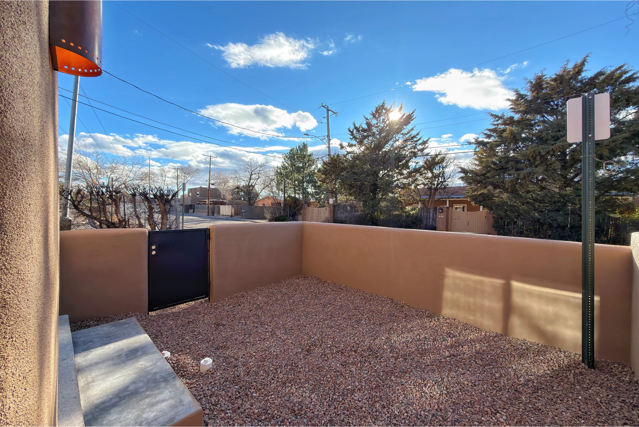 Sunny backyard with gravel ground and tan walls under a blue sky.
