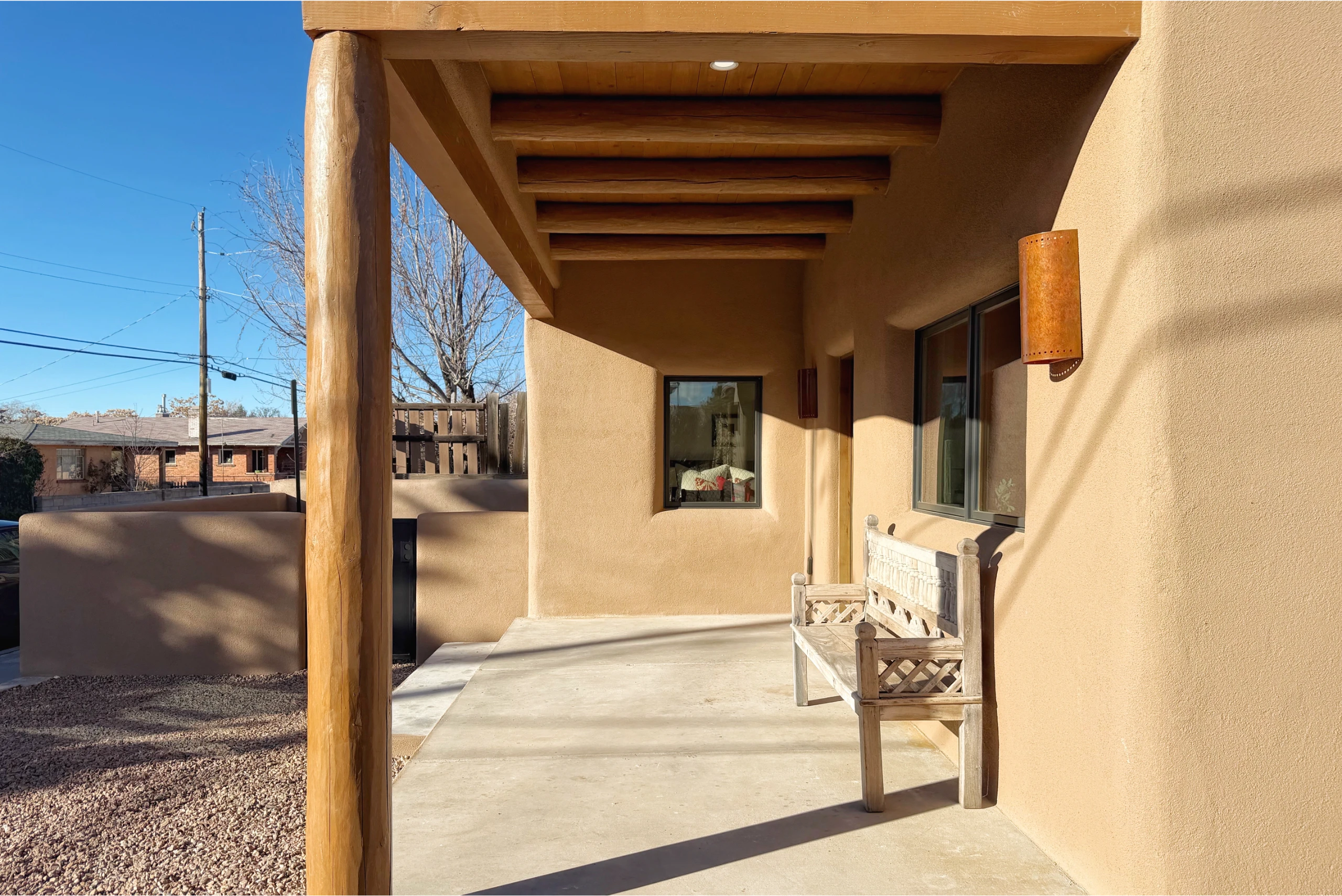A covered patio with wooden beams and bench seating in a sunny backyard.