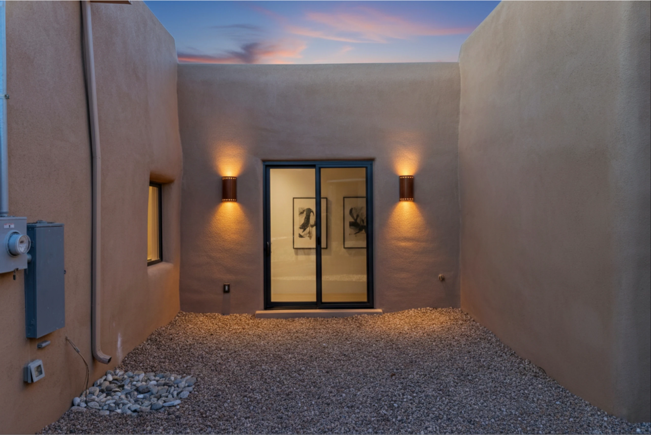 Modern adobe-style home entrance at dusk with warm lighting.